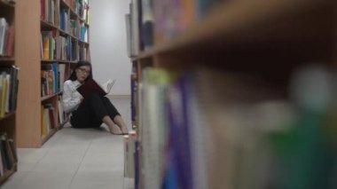 4k Genç Kadın Üniversite Kütüphanesi'nde Yerde Oturan Kitap Okuyor.