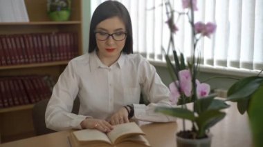 4k Güzel Kadın Öğrenci Üniversite Kütüphanesi'nde Masada Oturan Kitap Okuyor.
