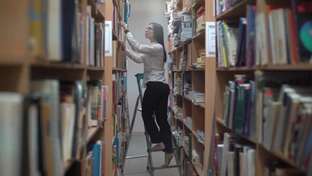 Γυναίκα Βιβλιοθηκάριος Επιλέγει Βιβλίο Από Ένα Ψηλό Ράφι — Αρχείο Βίντεο