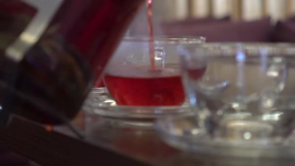 Lent mouvement versant la tisane rouge de la théière en verre dans la tasse 