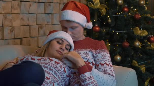 クリスマスツリーの隣のベッドに座って抱きしめる若い美しいカップル — ストック動画