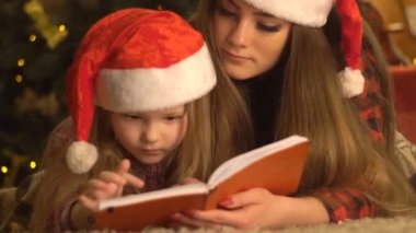 Noel ağacının yanında oturan ve kitap okuyan iki kız kardeş