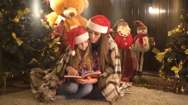 Μητέρα Και Κόρη Διαβάζοντας Βιβλίο Κοντά Στο Ξύλινο Χριστουγεννιάτικο Δέντρο — Αρχείο Βίντεο