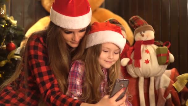 两个美丽的女孩有乐趣采取自拍在圣诞树背景 — 图库视频影像