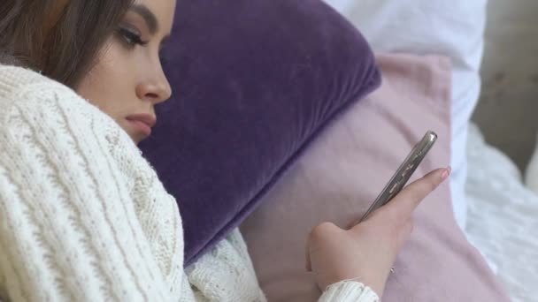 ベッドに横たわり スマートフォンでコンテンツを見ている若い女の子 — ストック動画