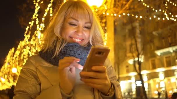 Vrouw Achtergrond Van Kerstverlichting Kijkend Naar Telefoon — Stockvideo