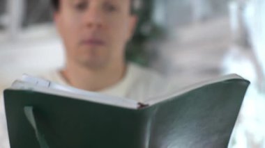 Kafede ilginç bir kitap okuyup yüzünü bununla kaplayan dalgın bir adam.