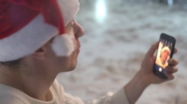 Gülen komik adam, Noel şapkalı beyaz sırt çantasındaki akıllı telefondan selfie çekiyor.