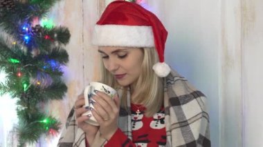 Sıcak kazaklı ve şapkalı kadın elinde çay fincanıyla oturuyor. .