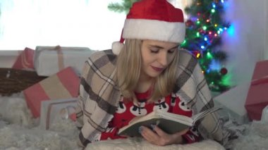 Genç bir kadın elinde bir kupa çay ve yılbaşı içeceği içinde bir kitapla yatıyor..