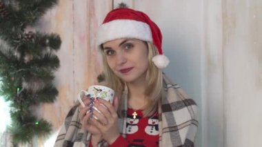 Sıcak kazaklı ve şapkalı kadın elinde çay fincanıyla oturuyor..