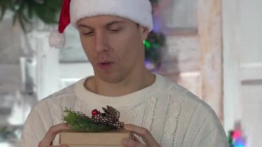 Noel şapkalı genç adam içinde küçük bir sürpriz olan hediye kutusunu açıyor.