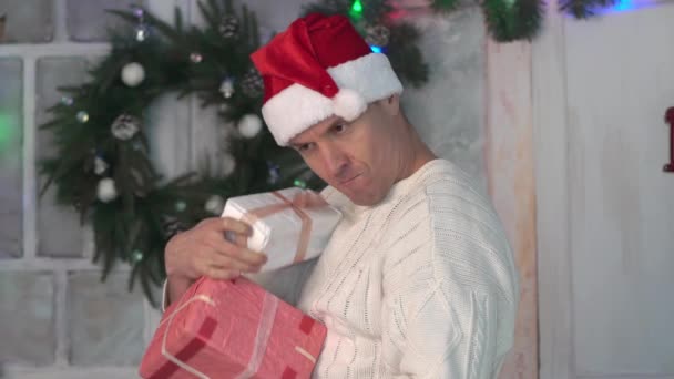 白い背景のスタジオで彼の手の中にクリスマスの贈り物を持つ男 — ストック動画