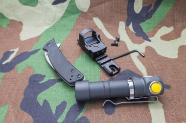 Military set on camouflage background from a flashlight, and the sight of the knife. clipart
