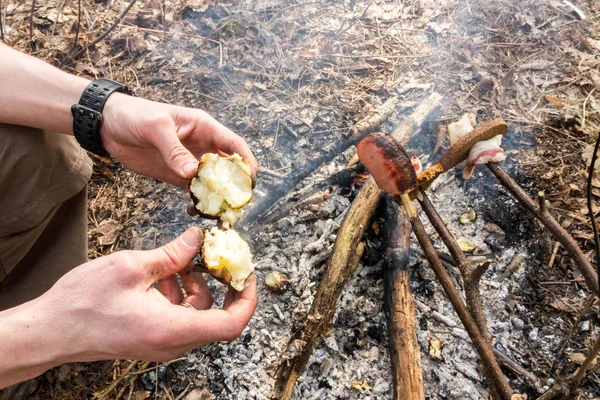 Man eating baked potatoes around the campfire.