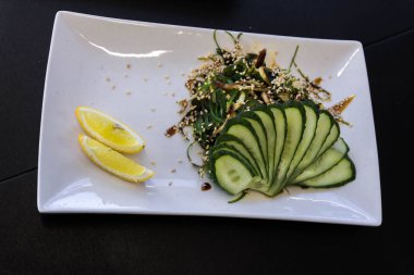 Meze. Soğuk aperatifler. Vejetaryen yemek. Salatalık, limon, susam. Beyaz bir tabak çanak. Dikdörtgen plaka.