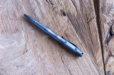 Gray metal handle for self-defense. Ballpoint pen made of metal. Wooden background from oak. clipart