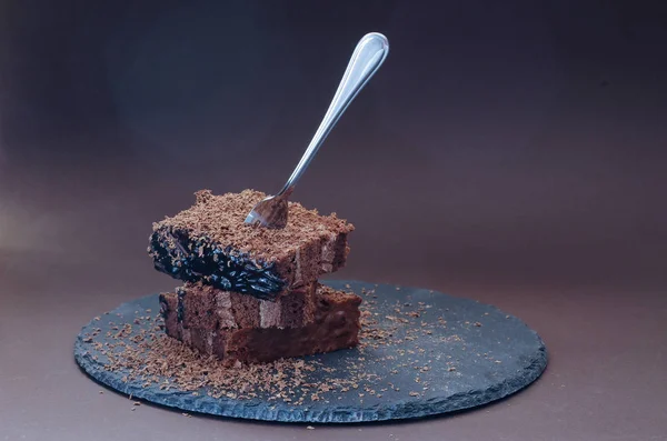 Slices of chocolate cake on a black background. A fork in the cake. Chocolate shavings.
