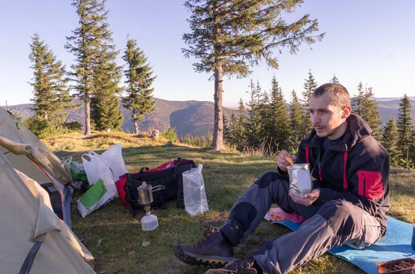 A man has lunch in the mountains. Cooking in a hike. Tourist lunch.