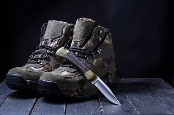 Camouflage boots with laces. Military boots and a knife. Hunting knife on the boot. Hunting still life.