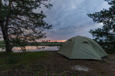 Gün batımı güneşinin arka planında turist çadırı. Nehir kıyısında turistik çadır.