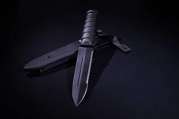 Cuchillo negro con funda de plástico. Cuchillo del ejército. Un cuchillo afilado con una sierra . — Foto de Stock