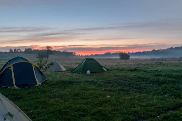 Tourist tents in the field. Tourist camp in the fog. Morning fog at sunrise. Morning in the field.