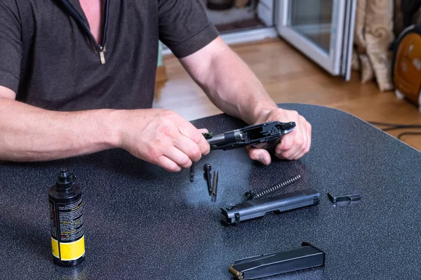 Lubricando el arma en casa. Mantenimiento del arma en casa. Cuidado con las armas. El hombre está limpiando el arma.. — Foto de Stock