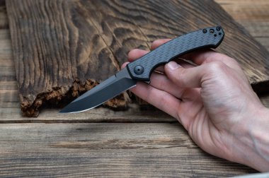 Karbon saplı katlanmış bıçak. Elinde küçük keskin bir bıçak var. Ön görünüm.