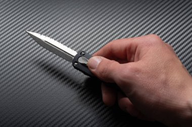 A knife with a double-sided sharpened blade. Automatic folding knife. Knife in hand. Black background. clipart