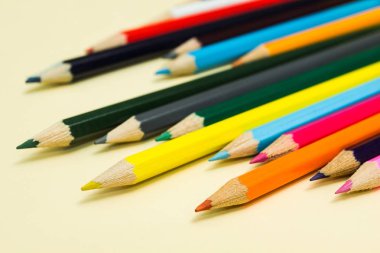 Pastel sarı arka plan üzerinde renkli kalemler