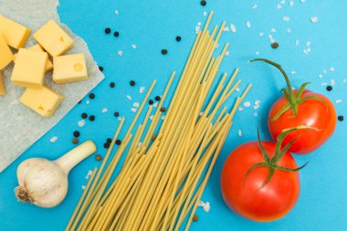 Makarna hazırlanması için malzemeler. Spagetti, peynir, domates, sarımsak, mavi bir arka plan üzerinde.