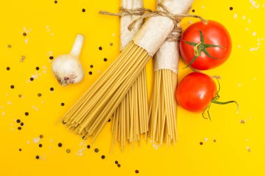Pişmemiş makarna rustik bir paket içinde sarı bir arka plan üzerine. Domates, sarımsak, biber ve tuz. Üstten Görünüm.