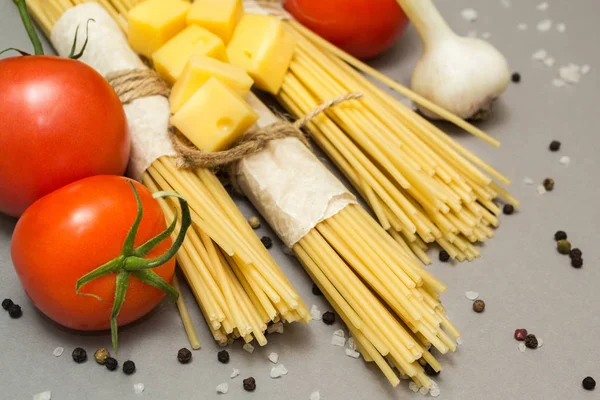 Pişmemiş makarna rustik bir paket içinde gri bir arka plan üzerine. Domates, sarımsak, biber ve tuz.