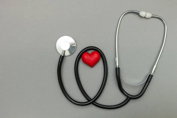 Medical stethoscope and red heart isolated on a gray background.