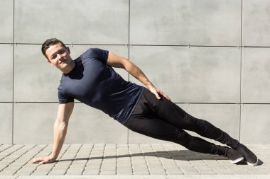 Güçlü genç adam açık havada bir gri arka plan duvar üzerinde Fitness yapıyor