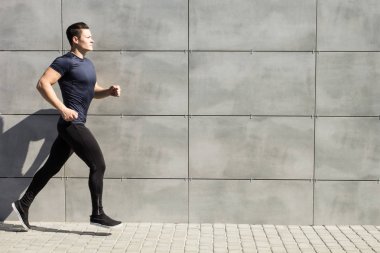 Genç bir adam bir gri duvara kentsel çalışır.