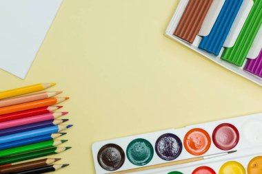 A yaratıcılık ve çizim için ayarla: suluboya boya, hamuru ve sarı bir arka plan üzerinde renkli kalemler. Üstten Görünüm.