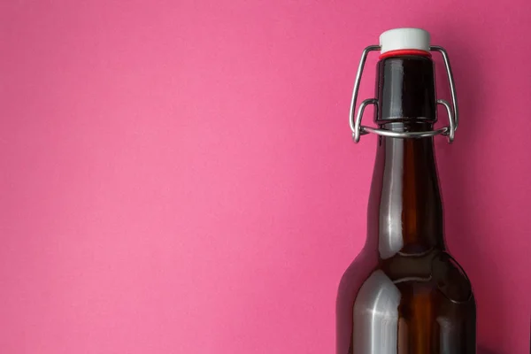 Old brown bottle with beer without label on a pink background, space for text.