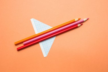 Kalem ve kağıt turuncu bir arka plan üzerinde uçak olmuştur. Okula dönüş.