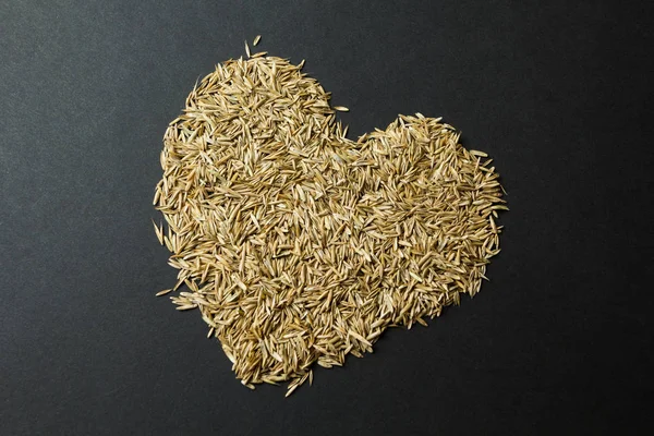 Corazón de semillas de hierba sobre un fondo negro . — Foto de Stock