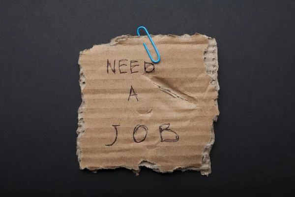 "Szüksége van munka" jelentkezik szakadt karton, fekete háttér. — Stock Fotó