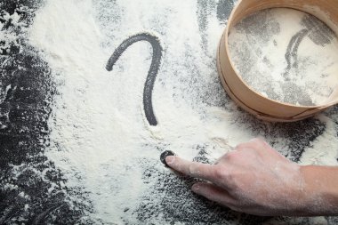 Bir kadın eli un üzerinde bir soru işareti çizer. Elek un için bir