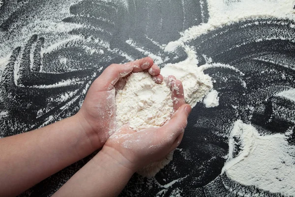 De handen van kinderen houden een handvol bloem op een zwarte achtergrond. — Stockfoto