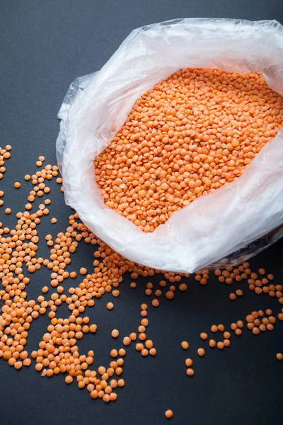 Lenticchie arancioni contadine biologiche in un sacchetto di plastica su uno schienale nero — Foto Stock