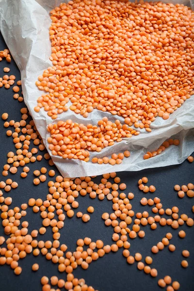 Red grains of lentils scattered from the package on a black back
