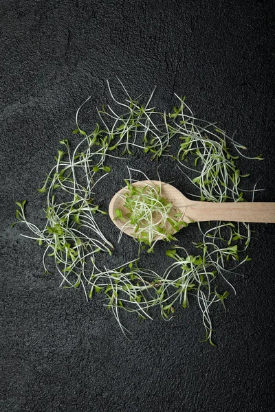 Uma colher de madeira em um fundo preto com micro verdes é uma comida — Fotografia de Stock