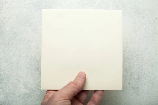 Beige square sheet of paper in a European hand, close-up. Mock-u