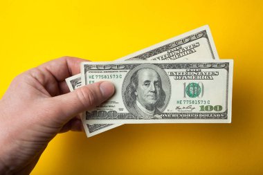 İki yüz dolar el üzerinde sarı bir arka plan, yakın çekim.