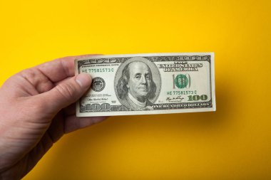 Sarı bir arka plan üzerinde elinde bir yüz dolar.